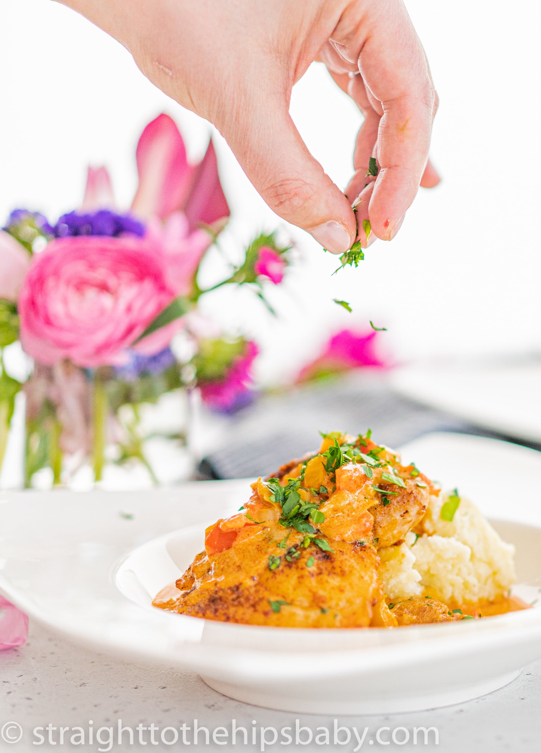 sprinkling chopped parsley over a plate of chicken paprika